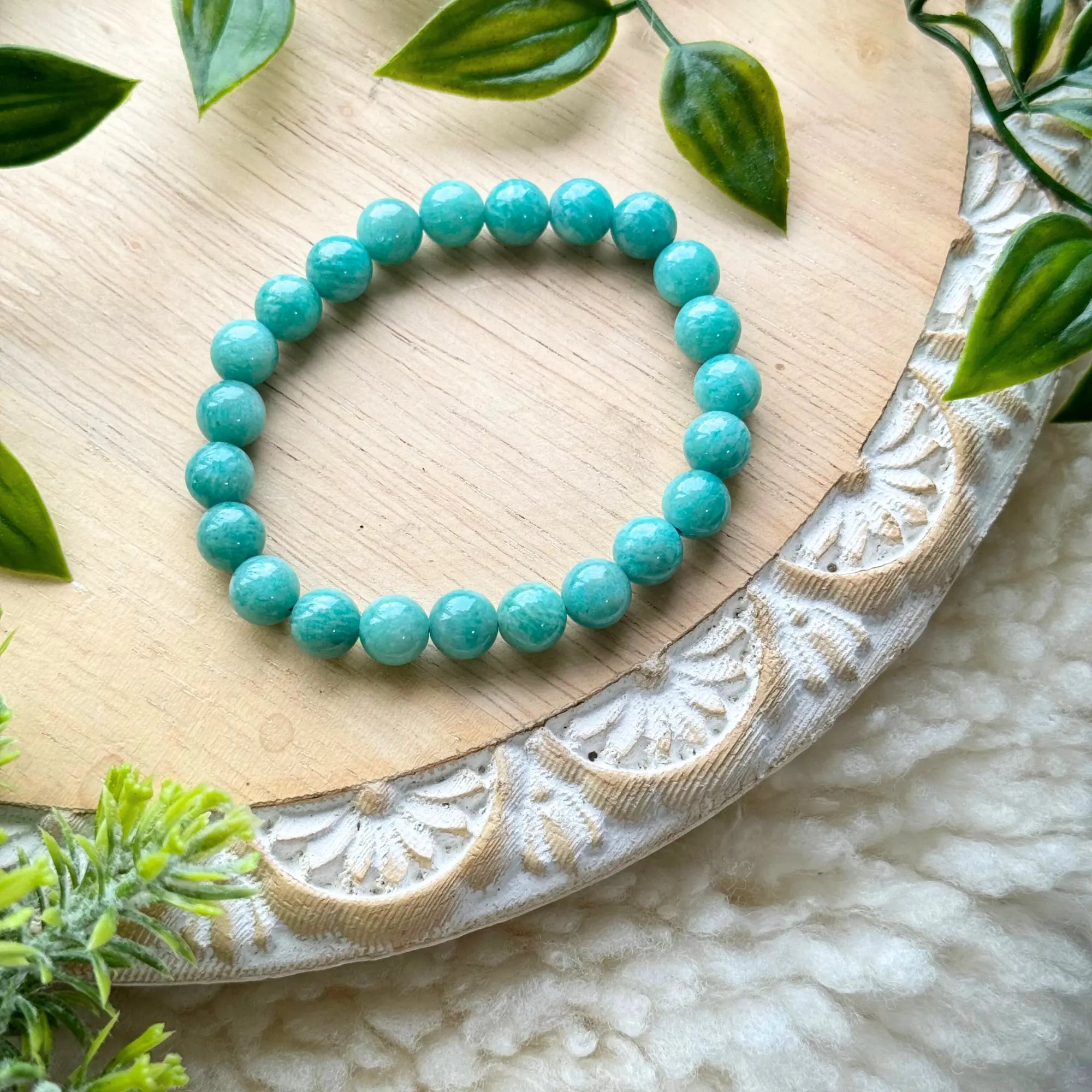 Turquoise colored beaded bracelet on a decorative wooden board with green leaves.