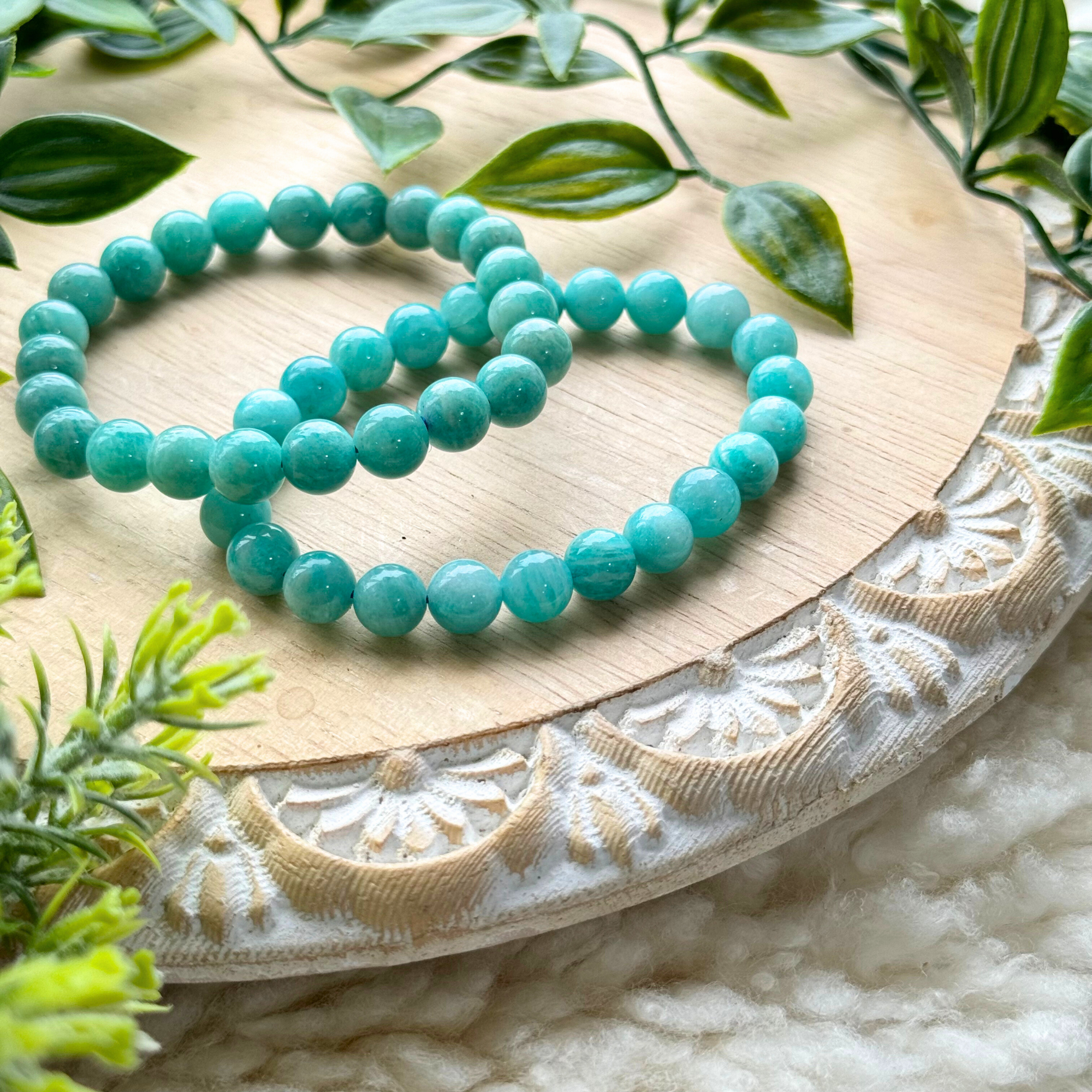A bracelet made of smooth, polished round beads in shades of aqua, teal, and pale green, displayed on a beige fabric with leaf patterns.